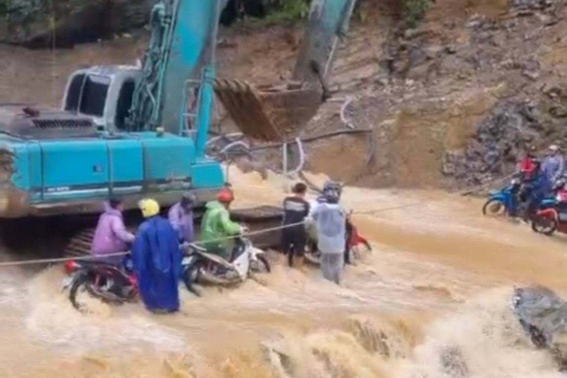 Hàng chục xe máy băng qua đoạn nước chảy cuồn cuộn tại khu vực hẻm Tu Sản thuộc huyện Mèo Vạc, Hà Giang có sự yểm trợ của máy múc (Ảnh: Cắt từ clip bạn đọc).